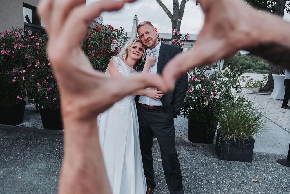 A heart shape made with hands frames a couple in wedding attire on their special day.