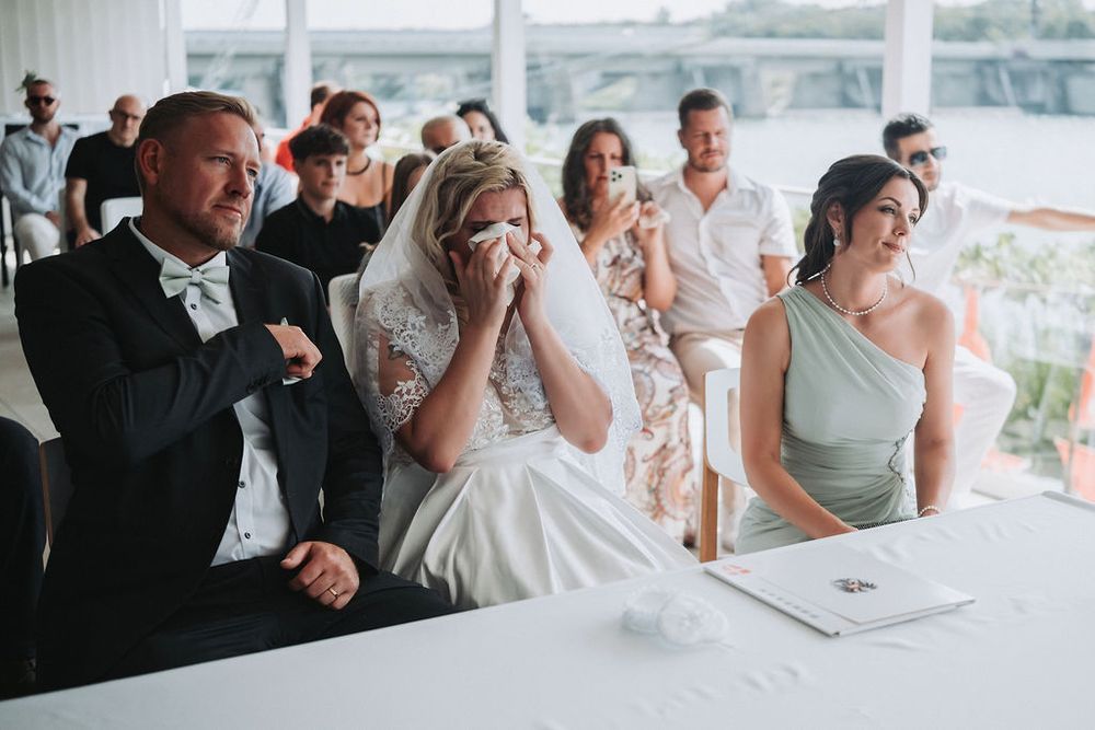 Wedding party members react with laughter and emotion during a celebration at a bright indoor venue.
