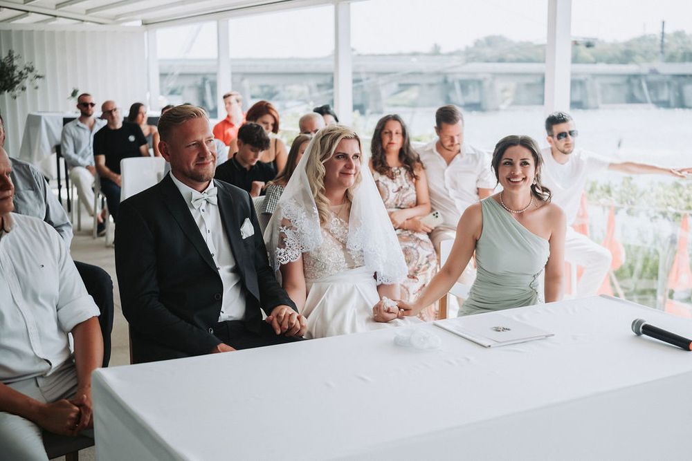 Wedding guests enjoy a celebratory moment at a bright reception venue with floor-to-ceiling windows.