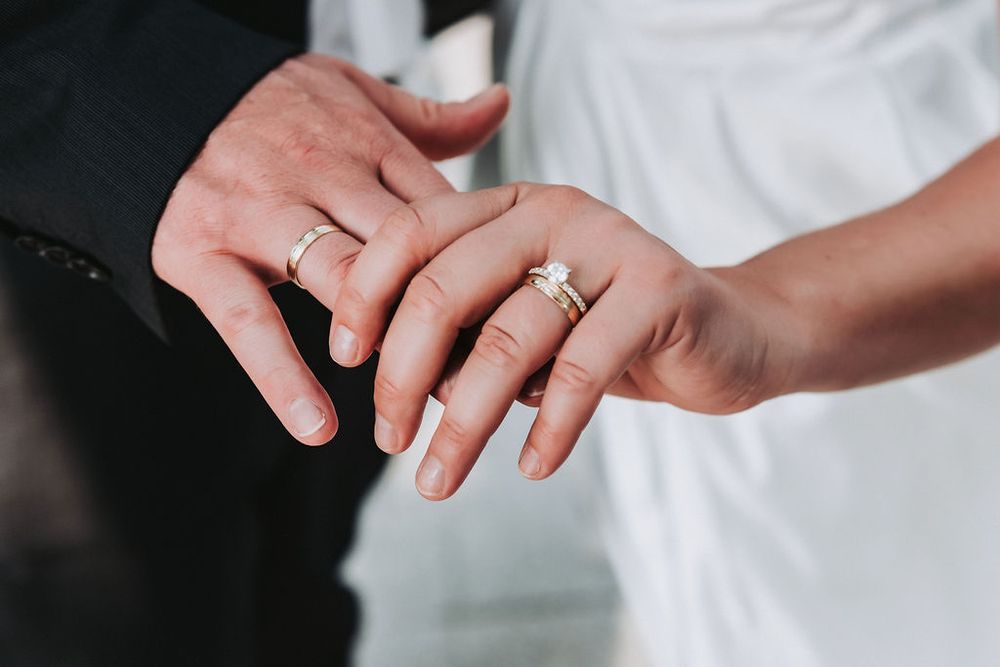 Close-up view of hands wearing elegant wedding rings against a white background.