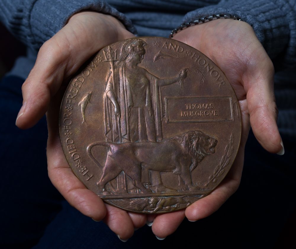 A pair of hands holding a large bronze World War I memorial death plaque, also known as a Dead Man's Penny.