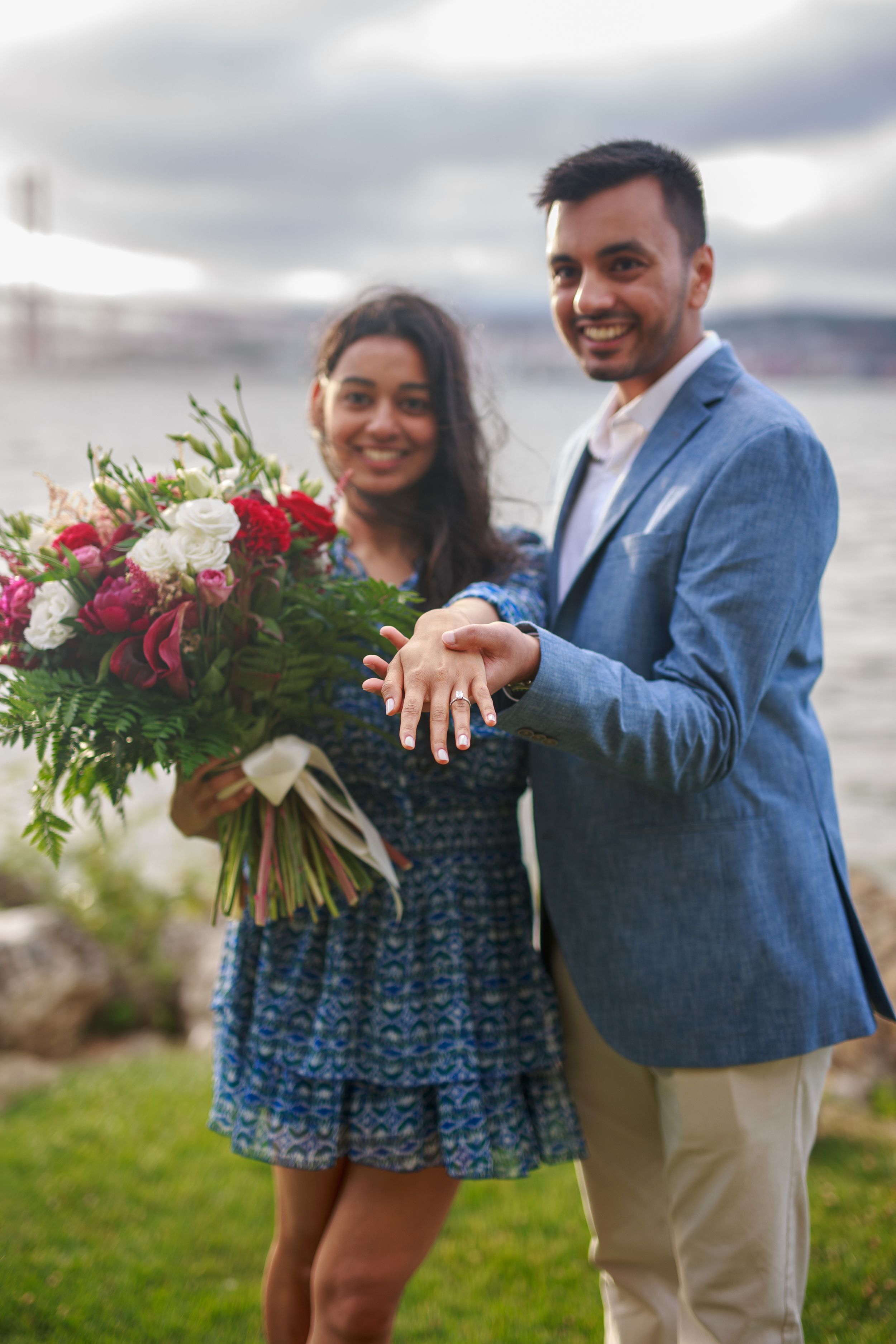 A couple celebrating their engagement with a beautiful floral bouquet by the waterfront.