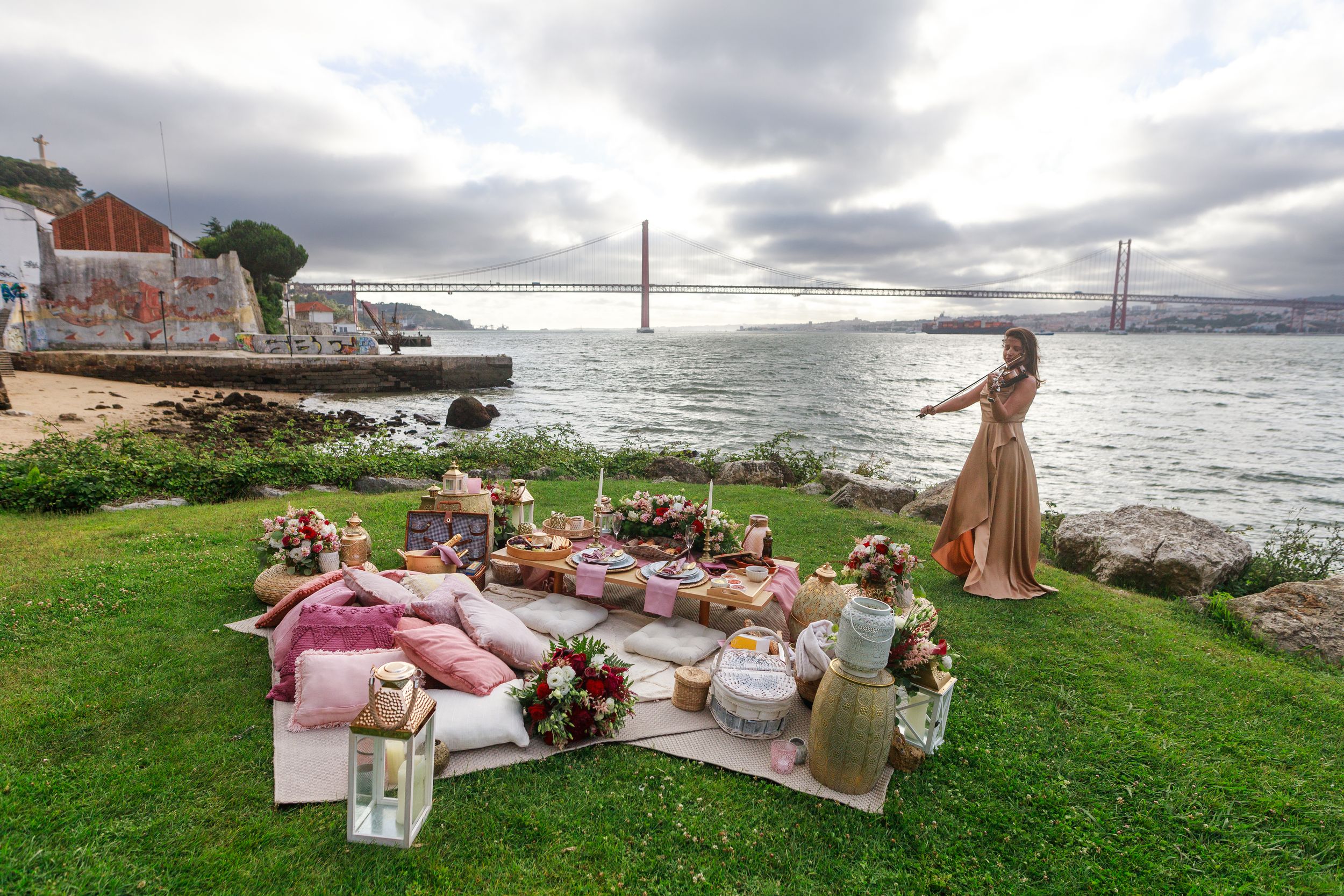 A picturesque seaside picnic setup with blankets and pillows overlooking the Golden Gate Bridge.