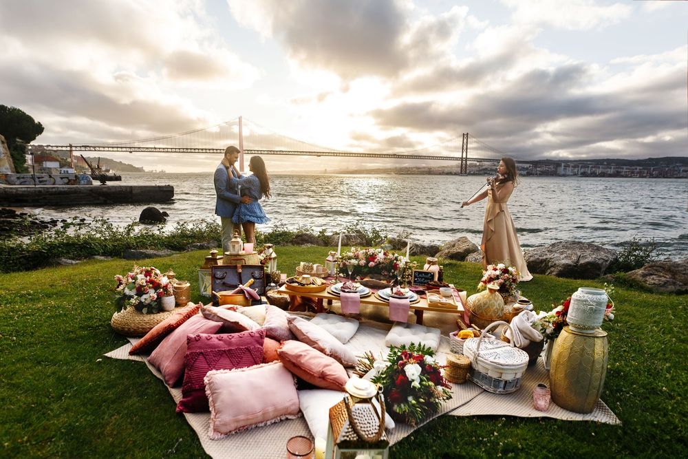 Romantic beach picnic setup with blankets, pillows and food baskets at sunset by the ocean.