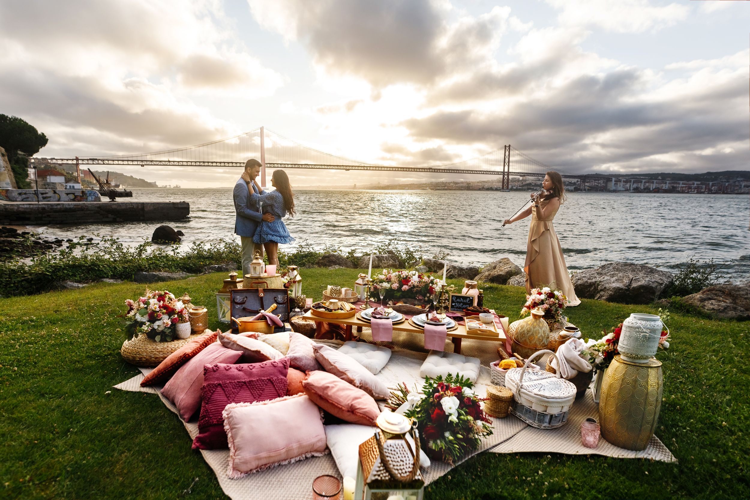 Romantic beach picnic setup with blankets, pillows and food baskets at sunset by the ocean.