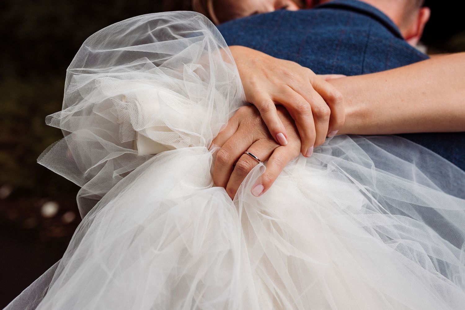 Close-up details of hands holding white tulle fabric at a wedding ceremony.