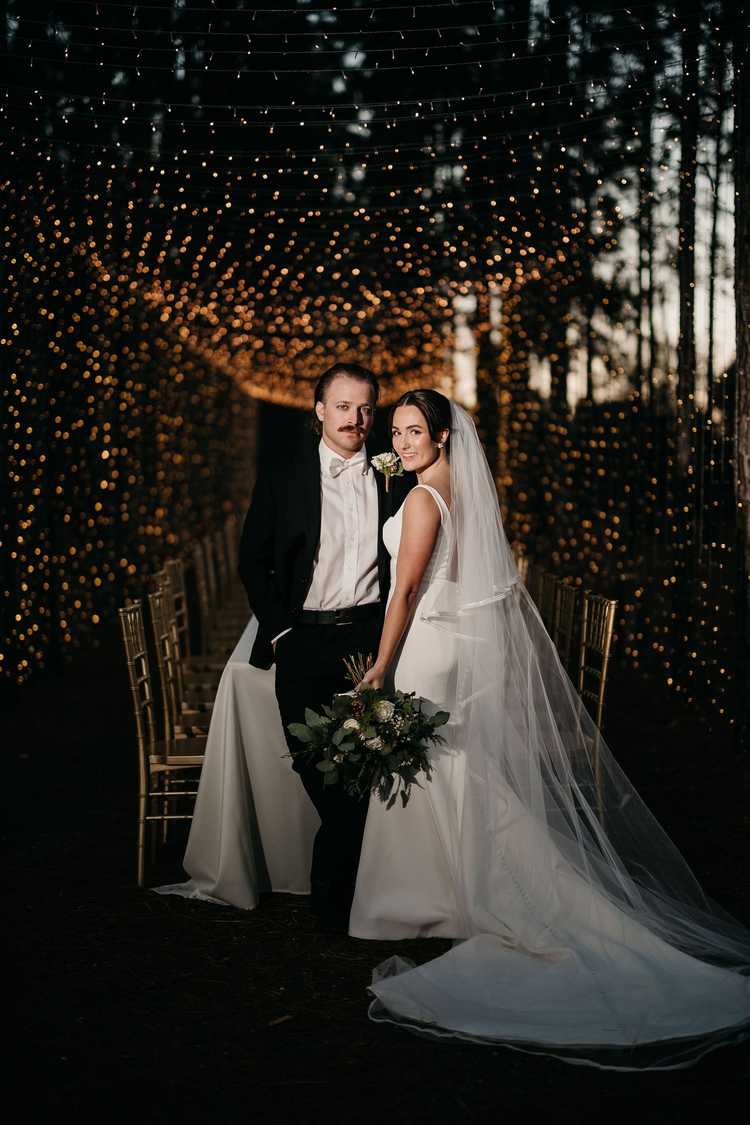 Wedding couple photographed at dusk with magical twinkle lights creating a romantic forest backdrop.
