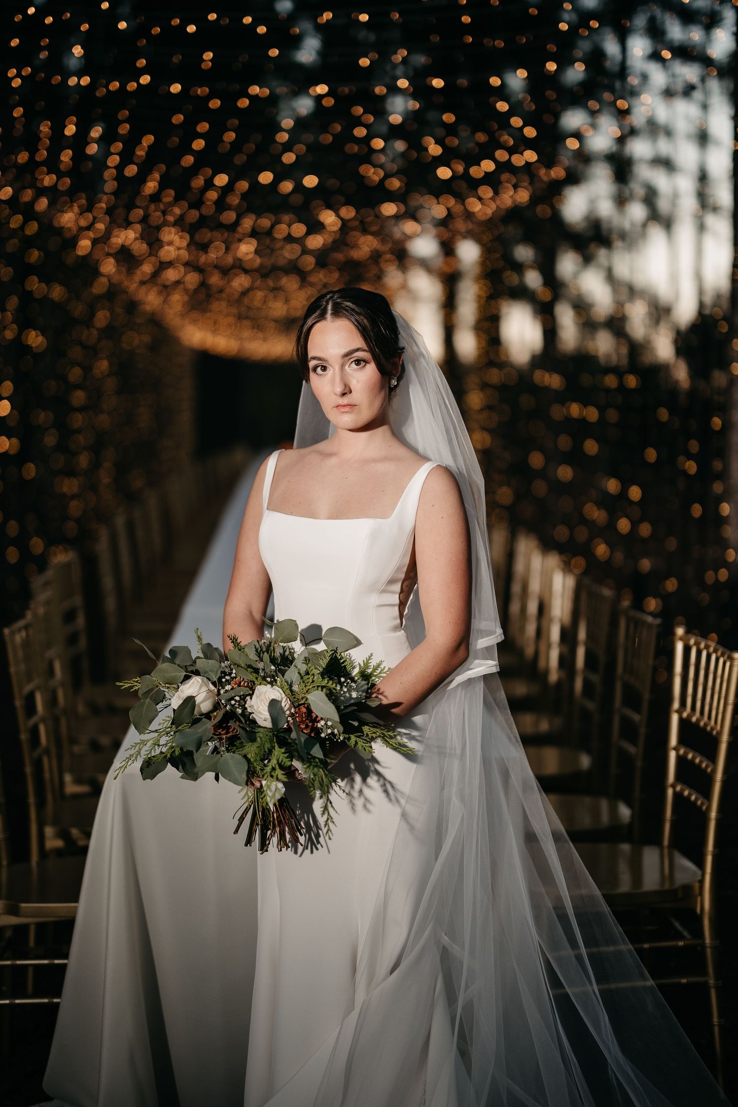 Bridal portraits with twinkling lights and forest backdrop showing elegant wedding dress and bouquet details.