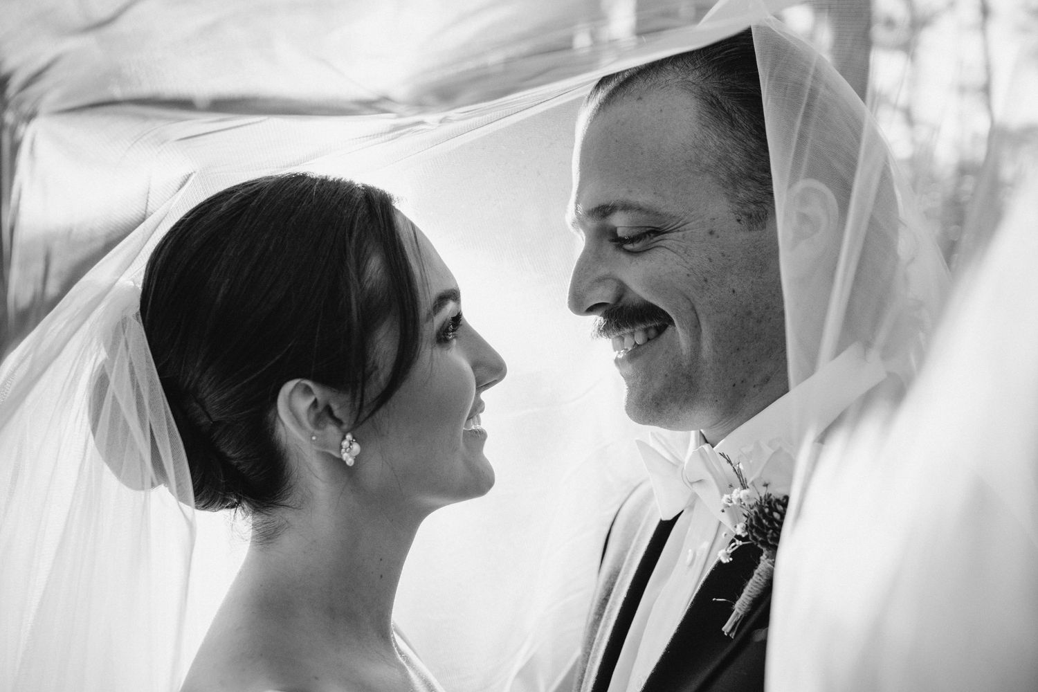 A romantic black and white wedding portrait series showing intimate moments between a couple under a veil.