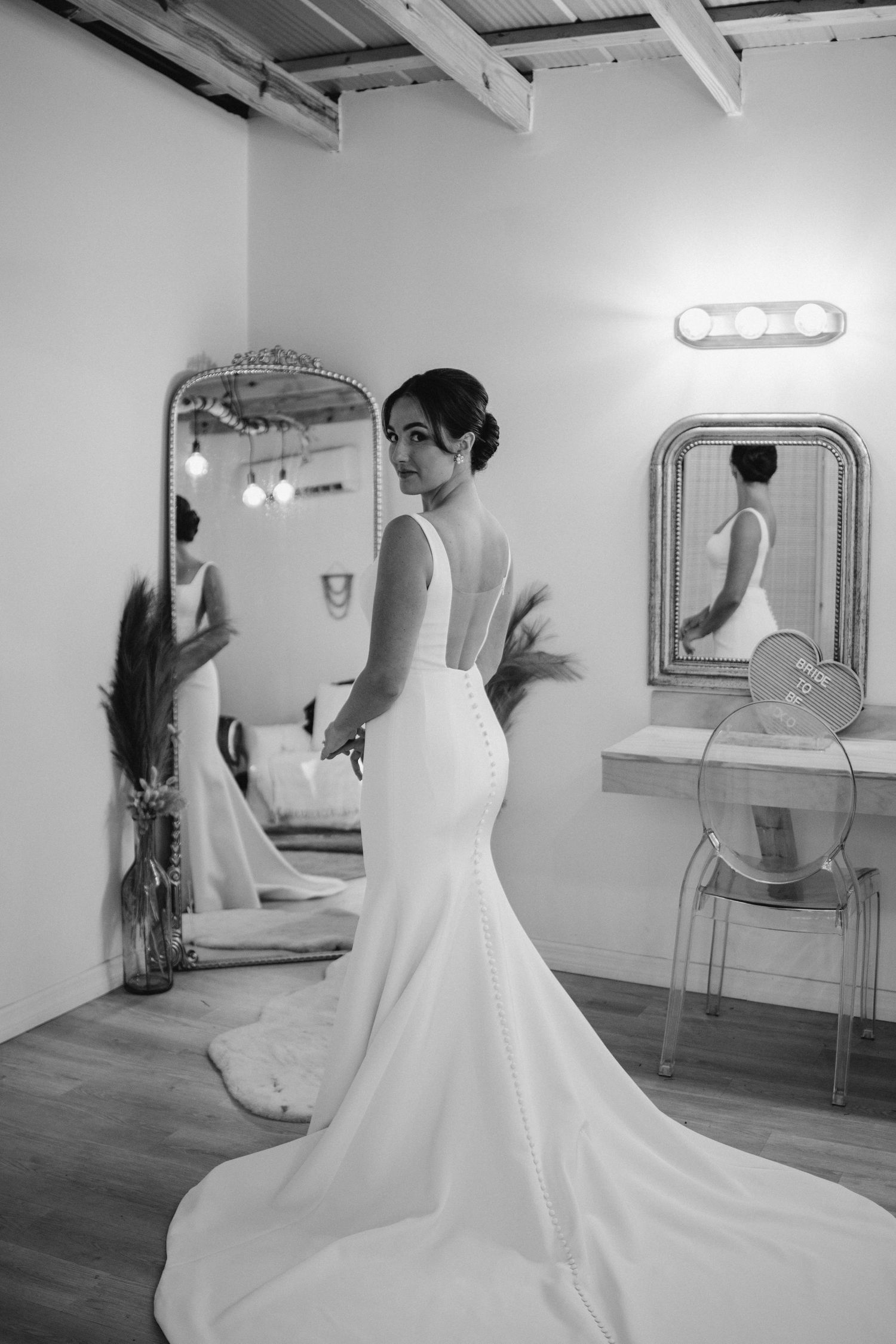 Black and white photos of a bride in a flowing dress posing in front of mirrors in a bridal suite.