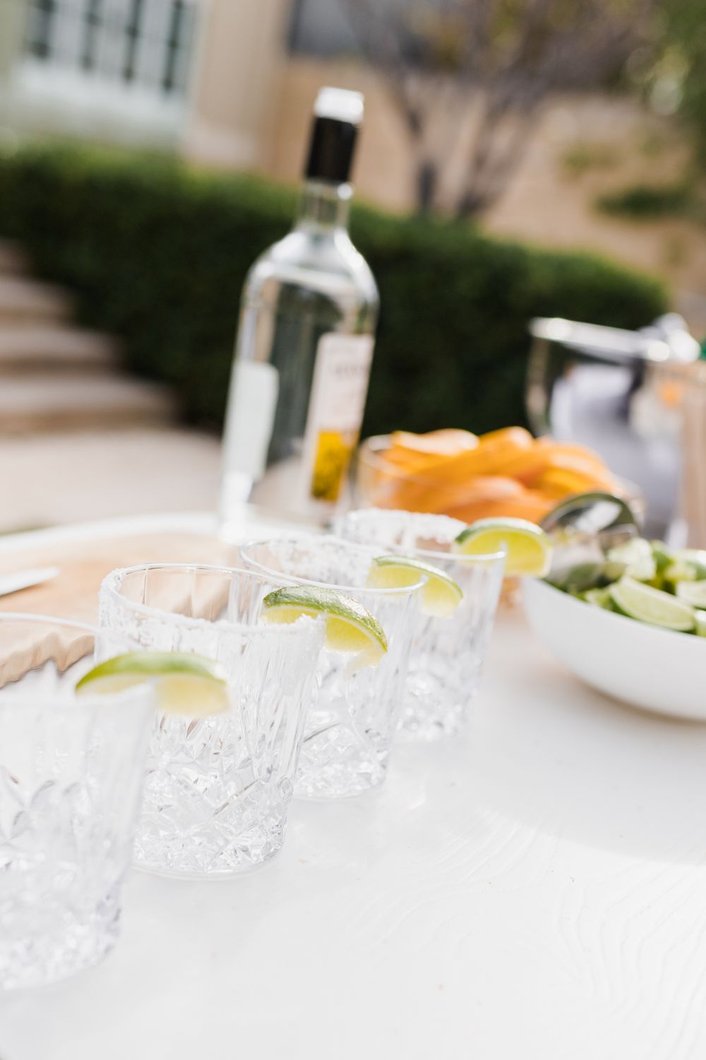 Close-up view of crystal cocktail glasses with lime garnishes lined up on a white tablecloth at an outdoor event.