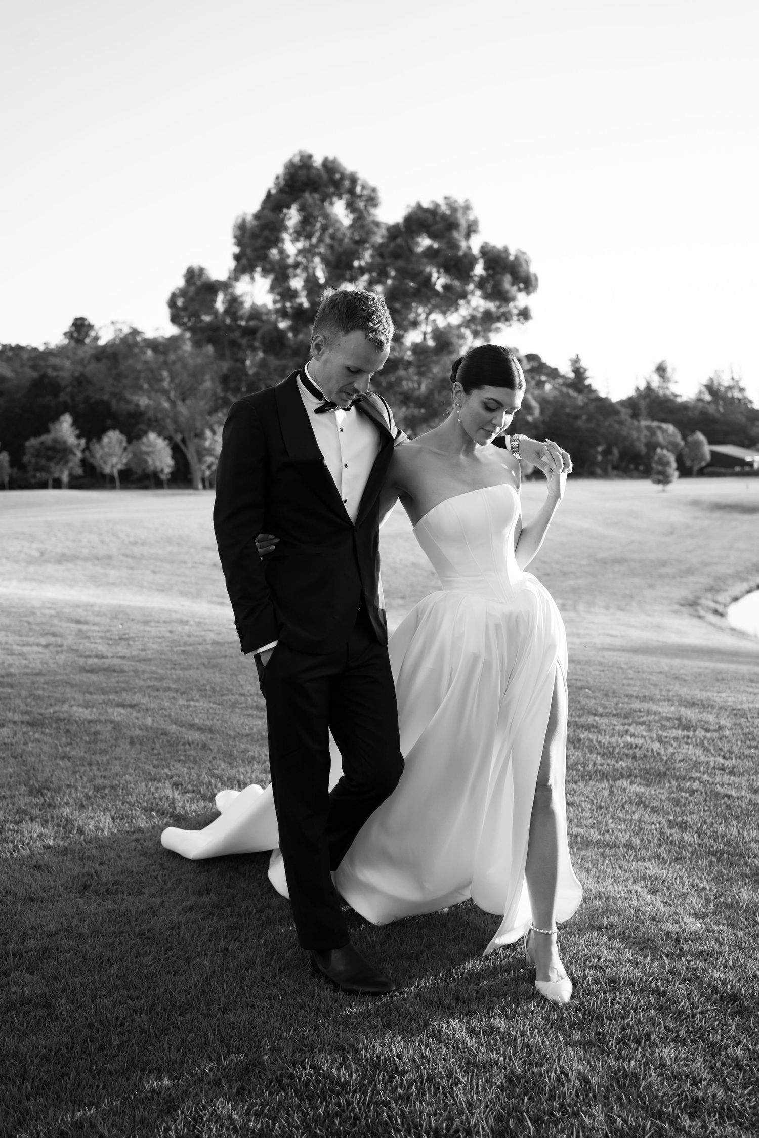 A romantic black and white wedding photo series showing a couple sitting together on a grassy hillside.