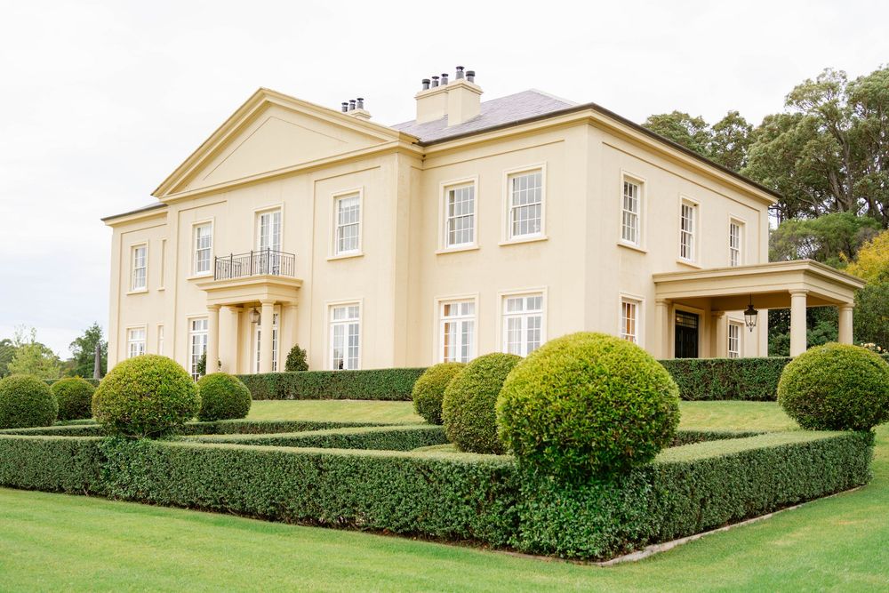 Elegant cream-colored Georgian mansion with manicured topiary gardens and hedges on a pristine green lawn.