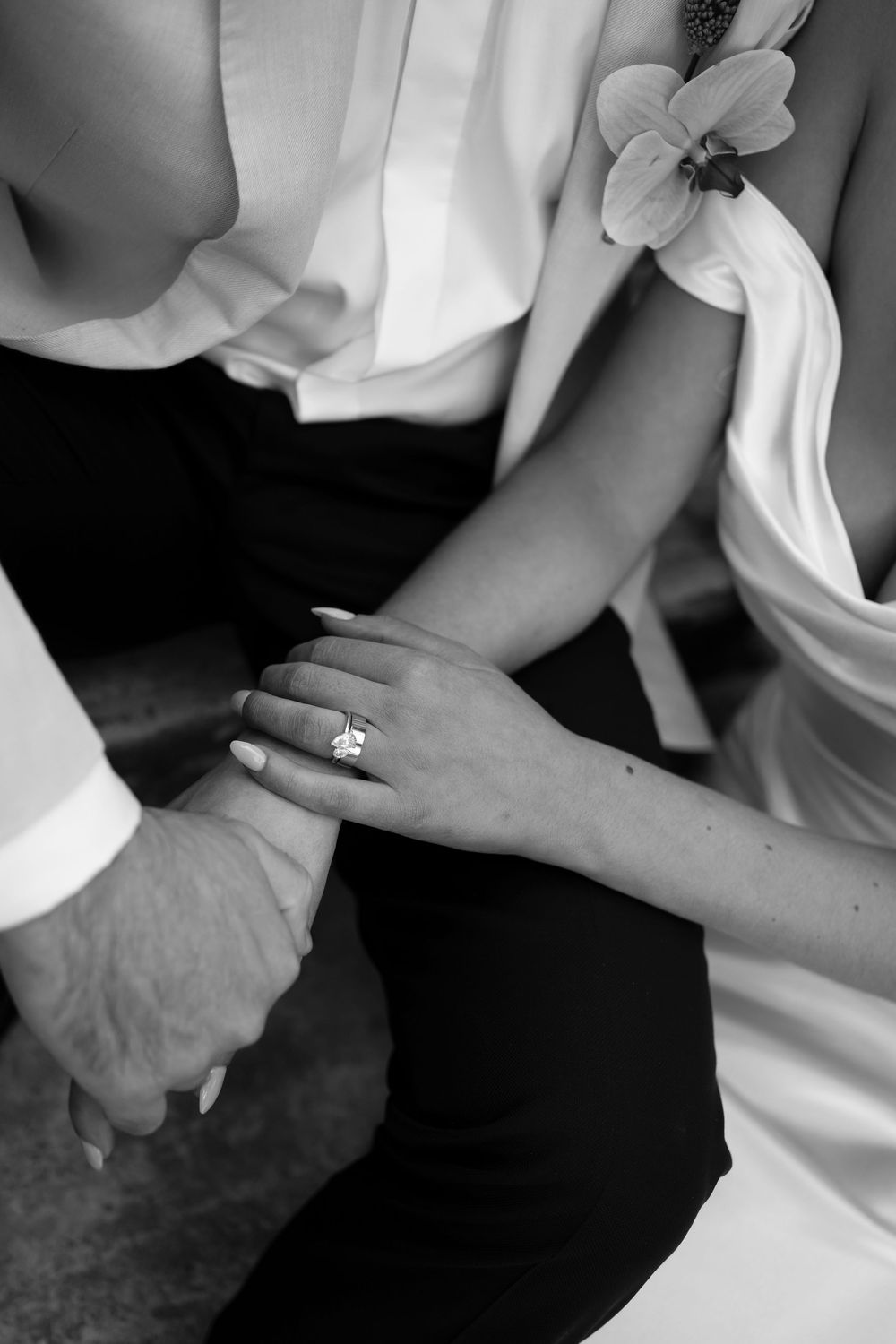 Black and white photo of a bride and groom holding hands, showcasing a elegant diamond engagement ring.