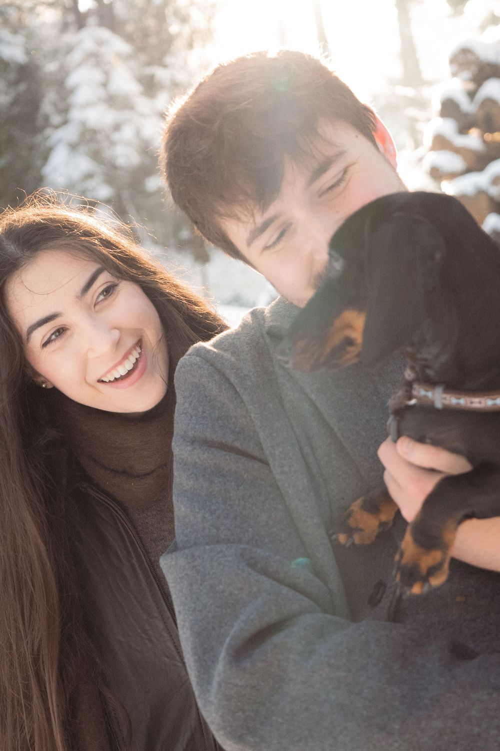 Playful winter moment with couple and black dog in the snow.