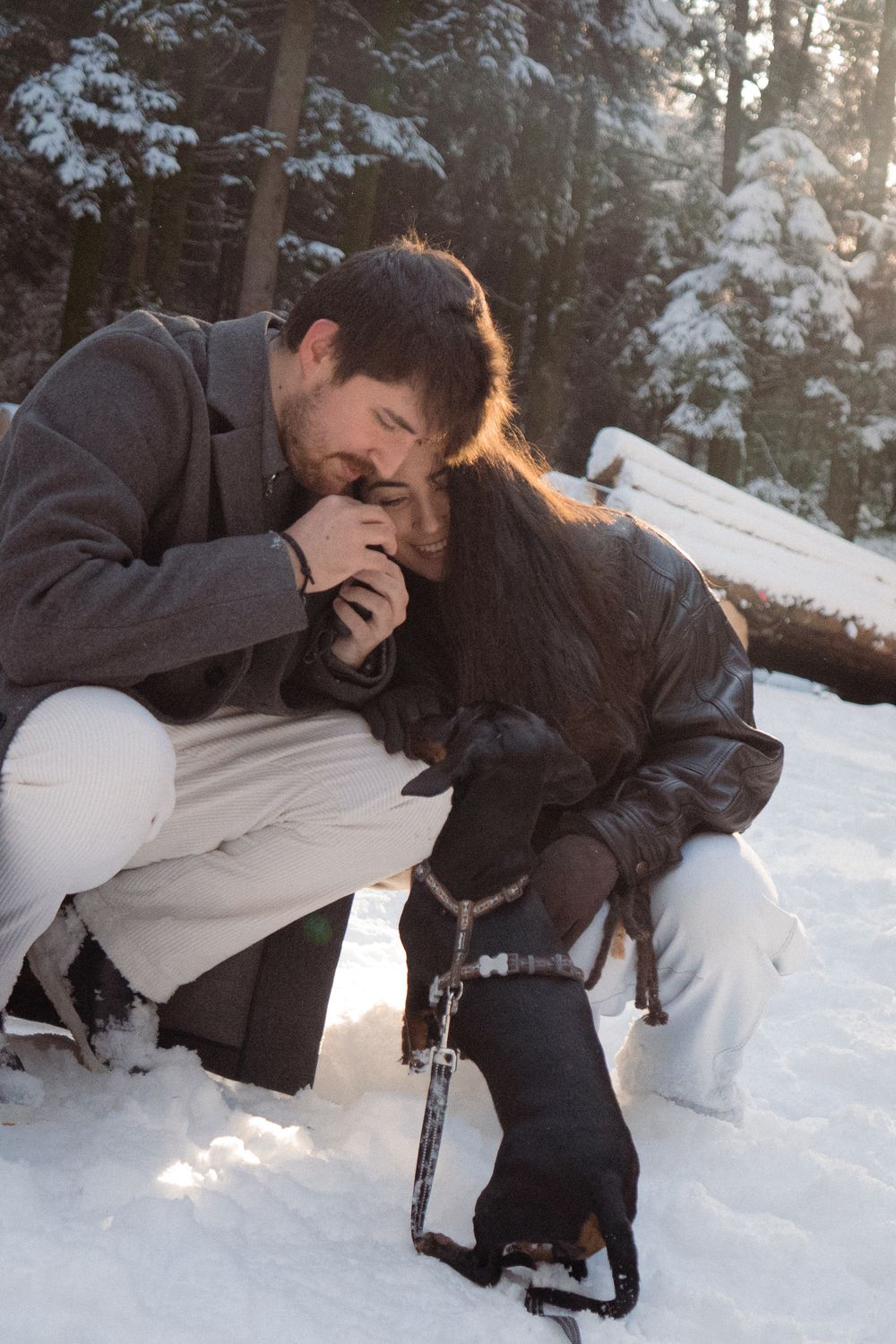Couple playing in deep snow with their black dog on a sunny winter day.