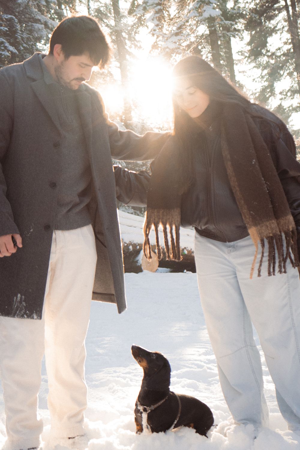Black dog and couple enjoying a winter walk through snowy forest.