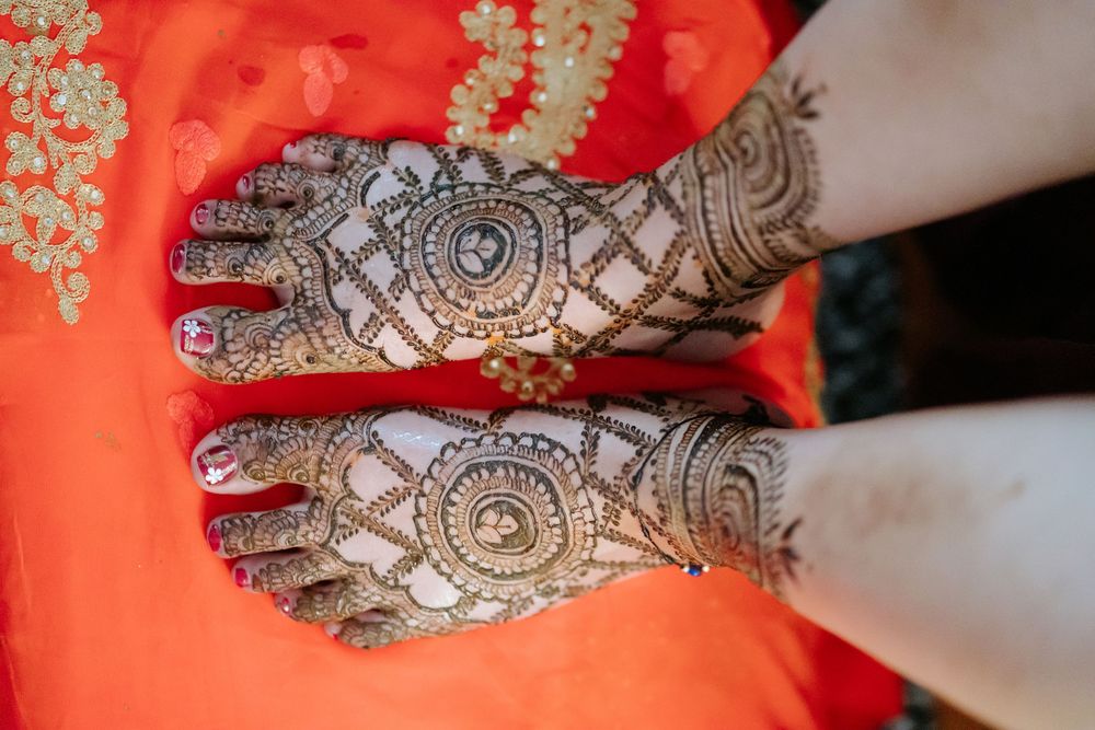 Close-up view of intricate henna designs being applied to hands against a vibrant red background.