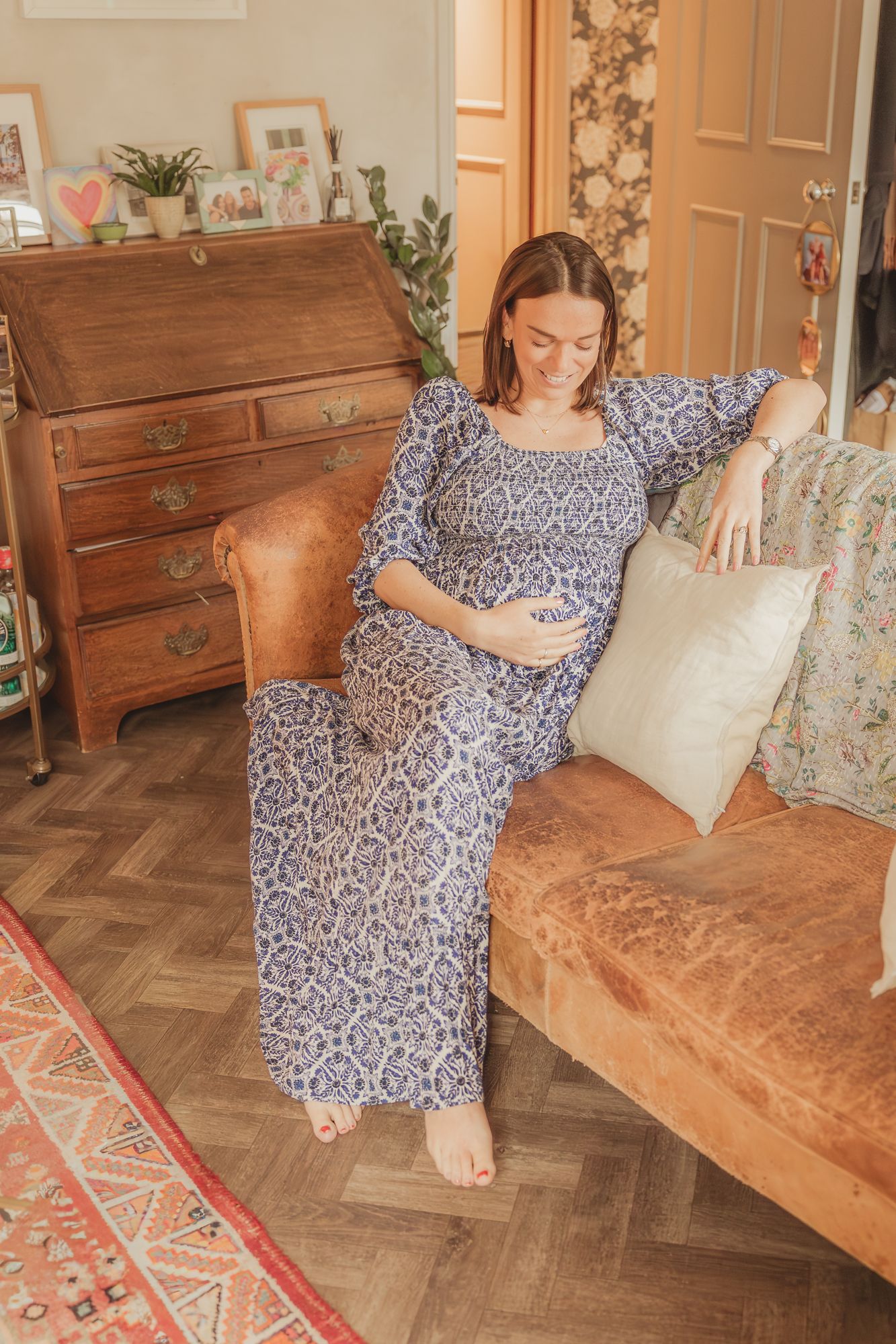 A blue and white floral dress is showcased on a leather couch with a patterned rug and wooden floor in a home setting.
