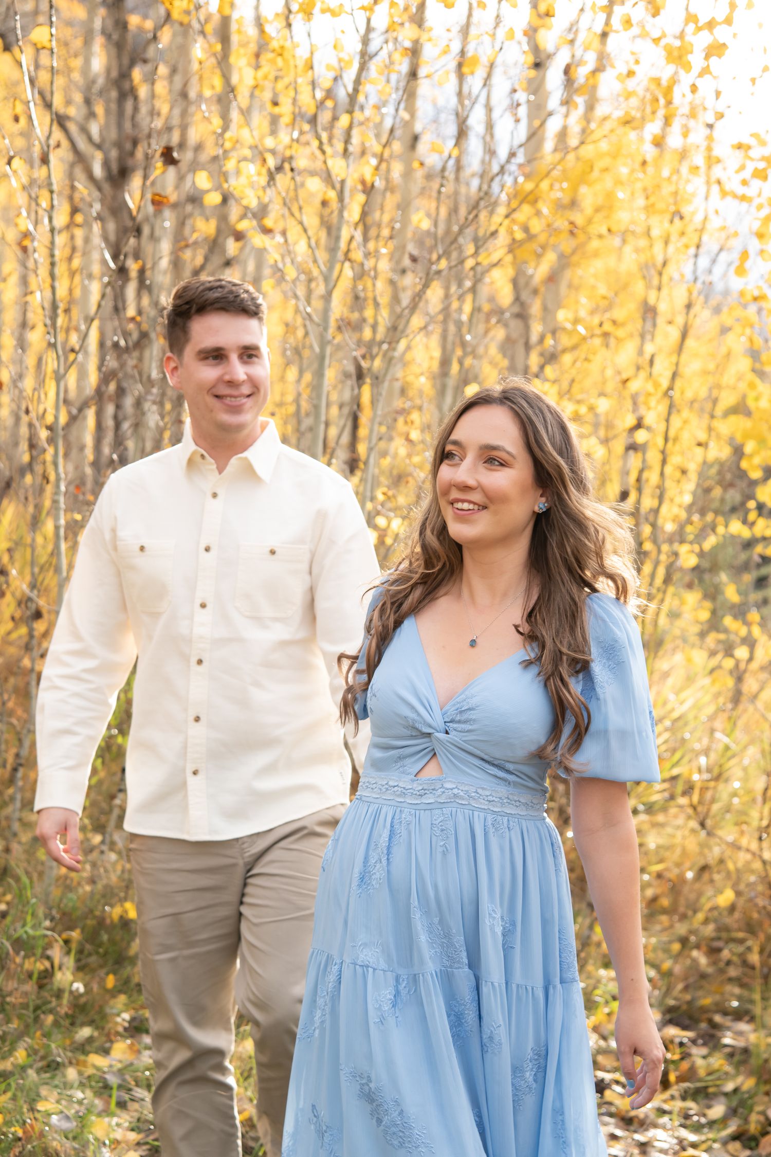 A couple in autumn aspen trees wearing white shirt and blue dress pose together among golden yellow fall foliage in Vail Colorado