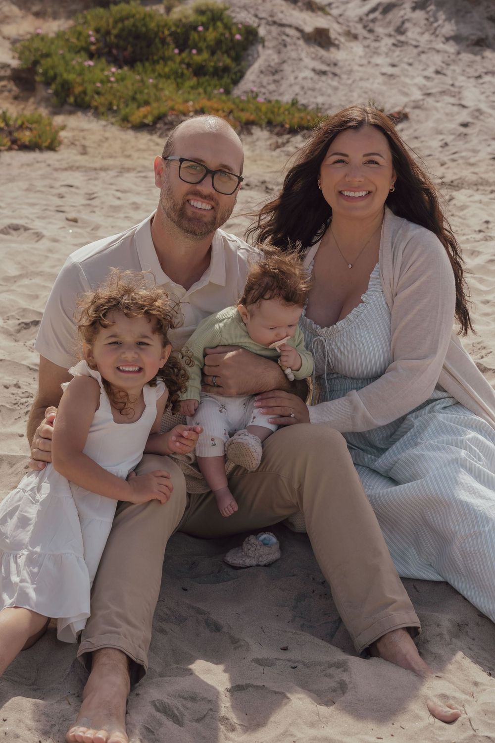 Family sitting together on sandy beach in casual attire enjoying a sunny day.