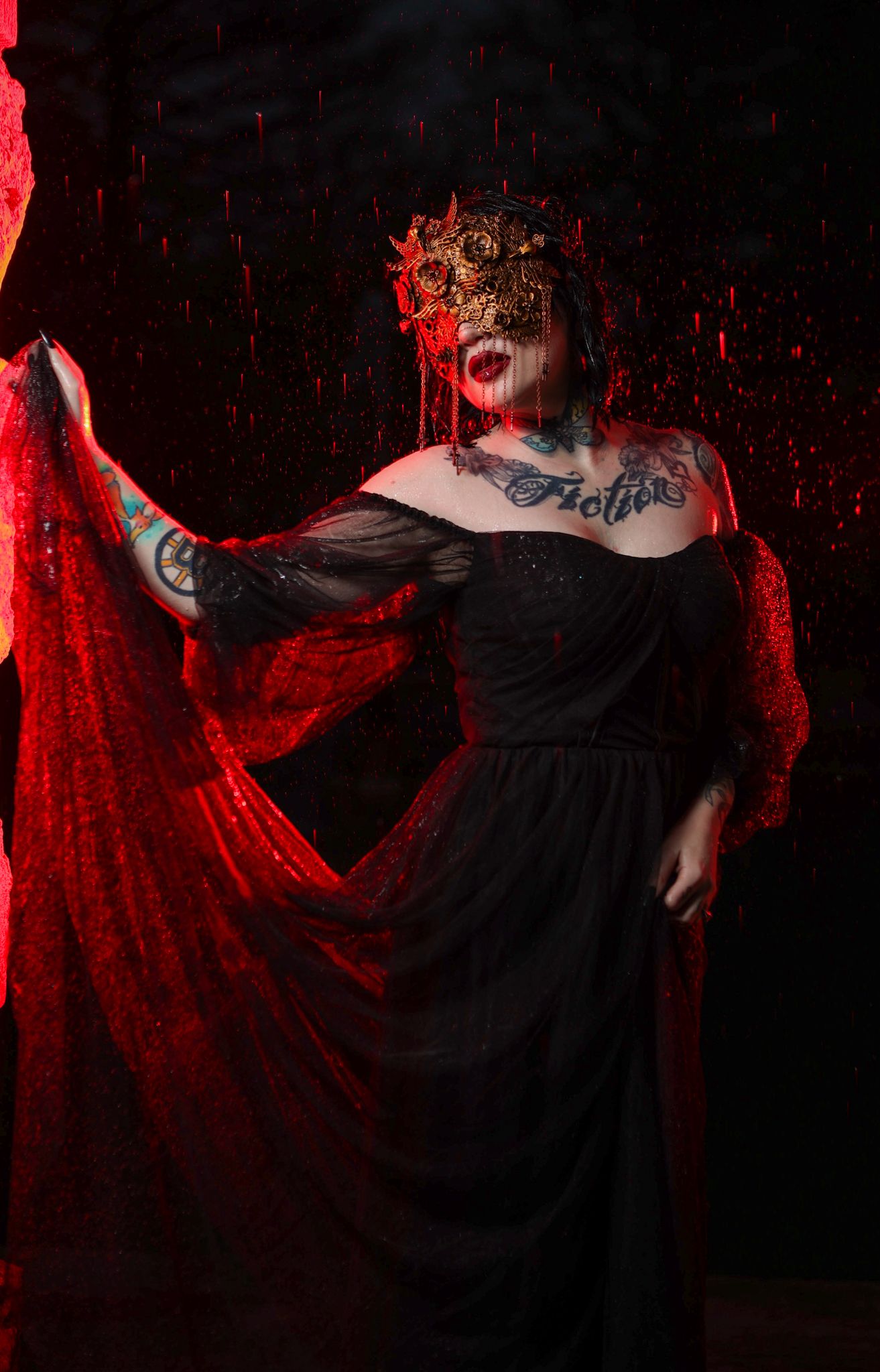 Dark dramatic portrait with red lighting showing person in black dress and ornate headpiece.