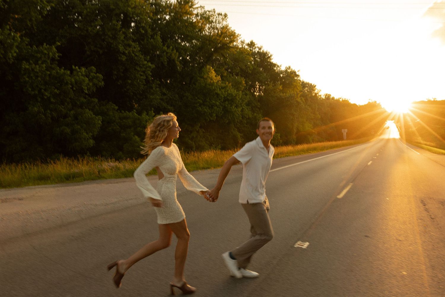 A couple running playfully down an empty road at golden hour.
