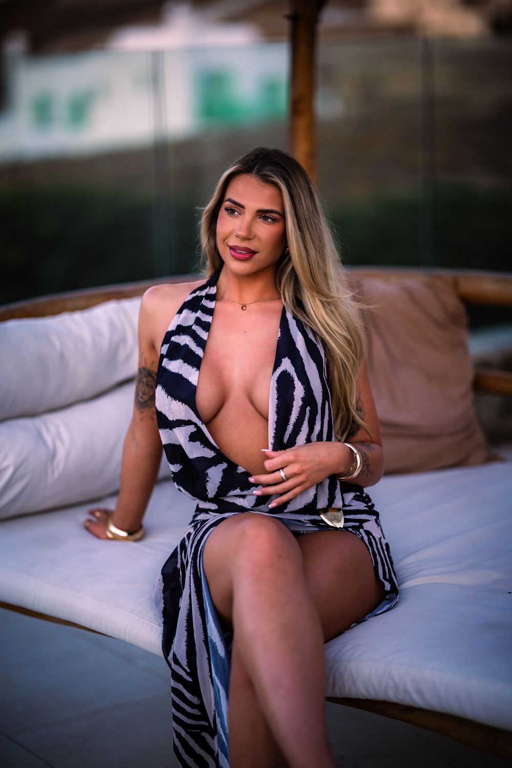 Model poses on white bedding wearing a navy and white striped dress in a boudoir photoshoot setting.