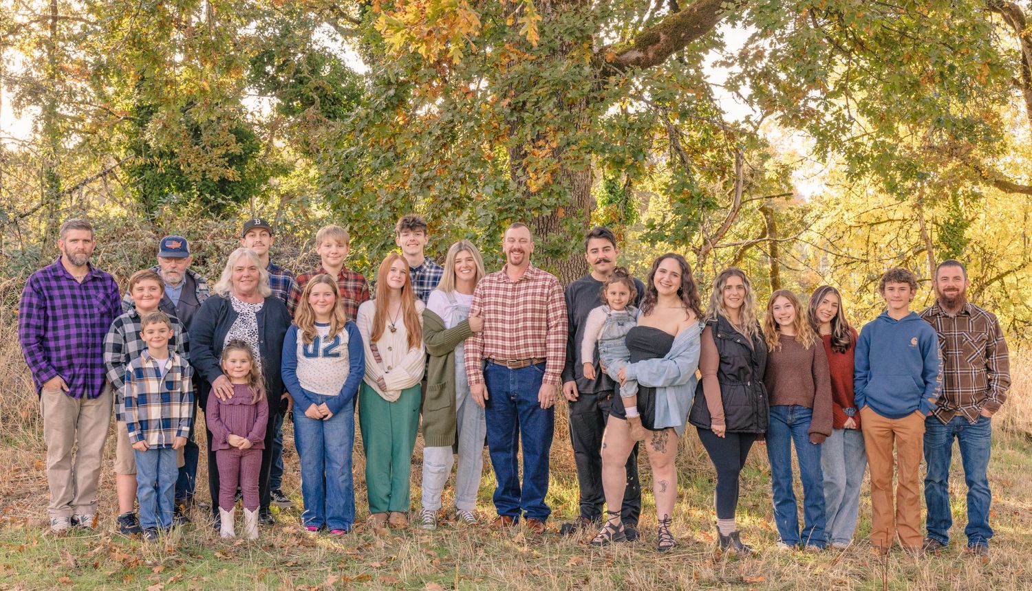 Large extended family portrait session outdoors with fall foliage in the background.