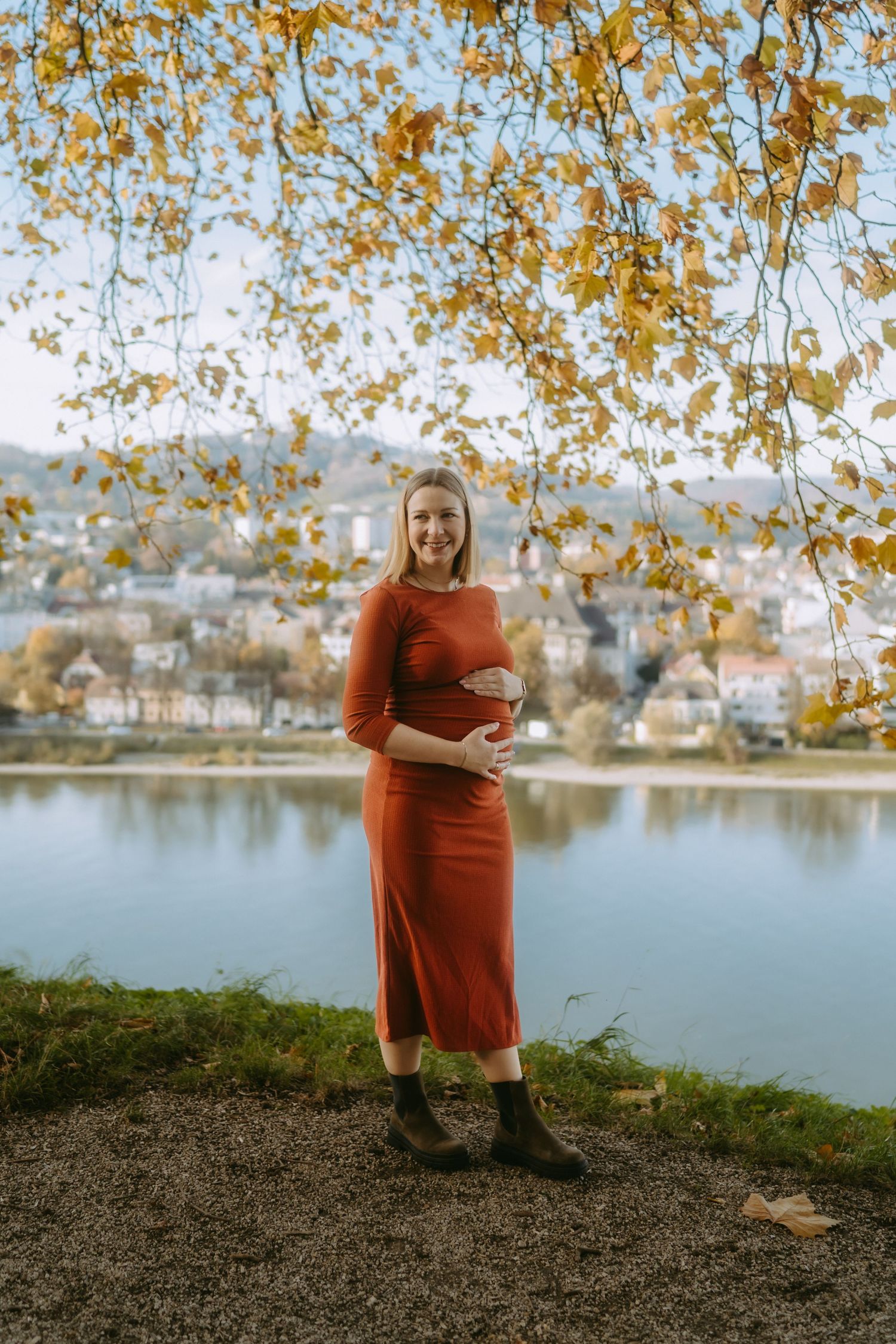 Frau steht unter einem riesigen Baum, sie hält ihren schwangeren Bauch in den Händen