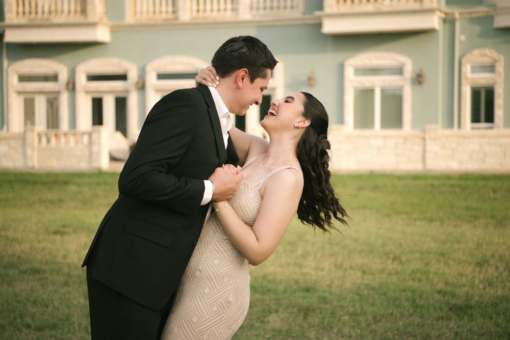 Couple shares an intimate kiss on the grounds of a luxurious estate with traditional architecture.