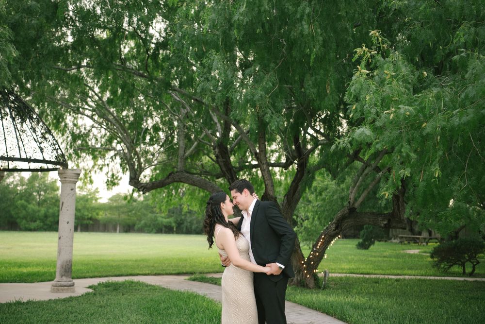 Romantic couple shares tender moment under lush green trees in garden setting.