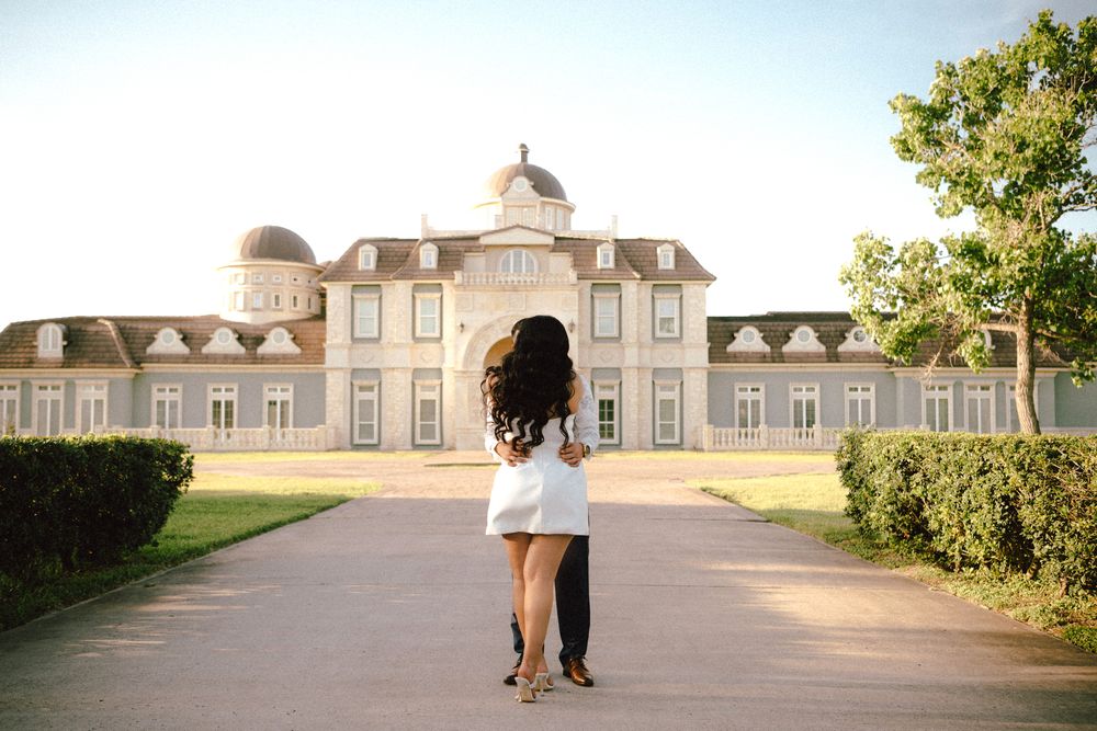 A couple stands together in front of a grand historic mansion with a domed roof and symmetrical architecture.