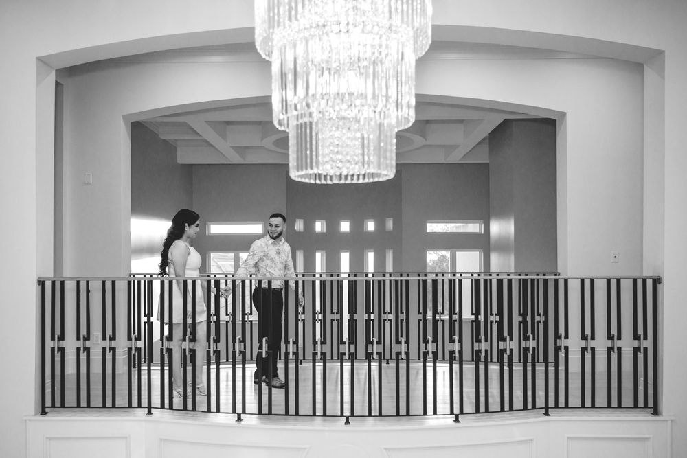 Modern crystal chandelier hangs in elegant white room with black railing details.