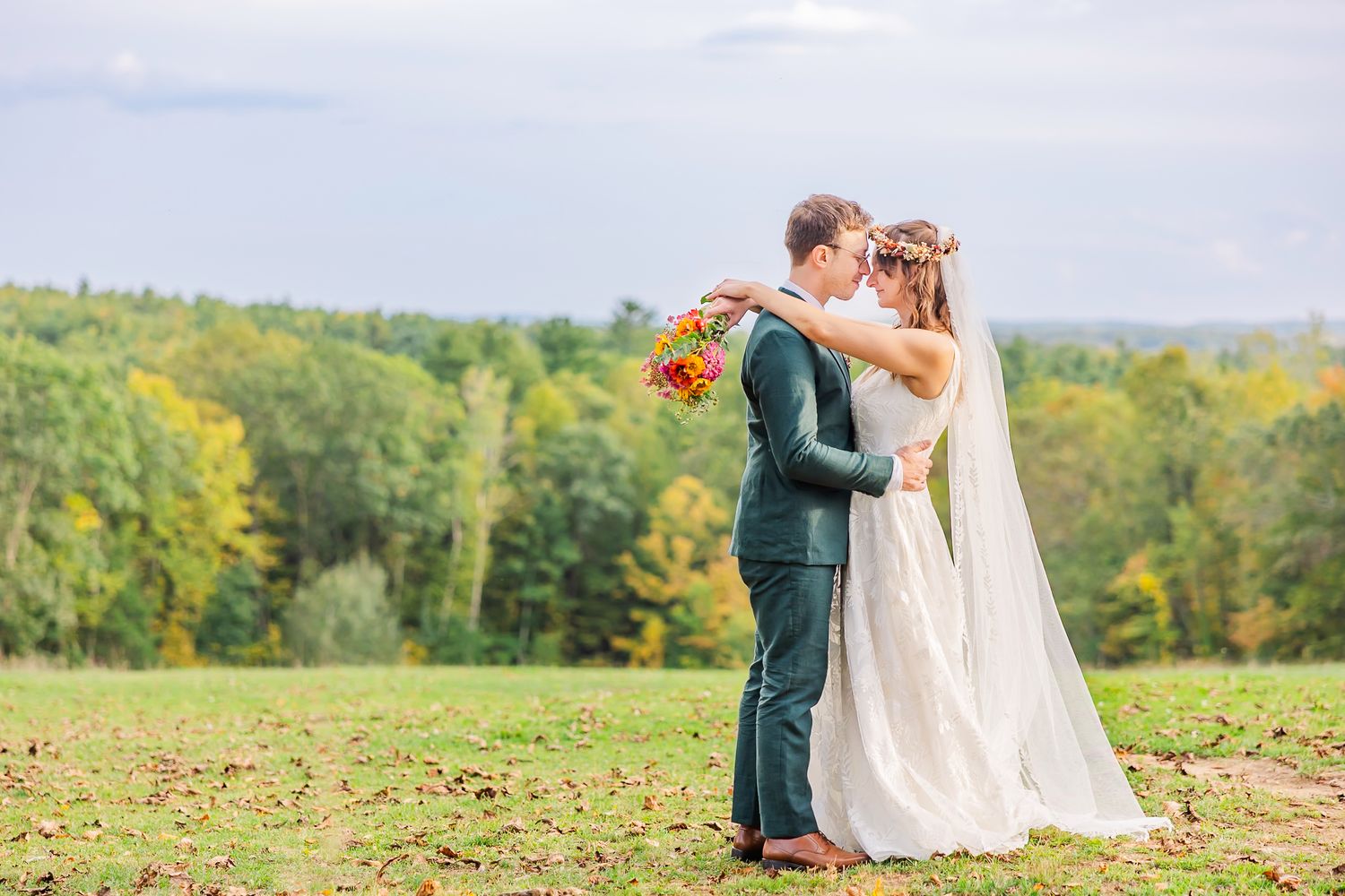 A couple shares an intimate moment on a hilltop overlooking a lush autumn forest landscape.