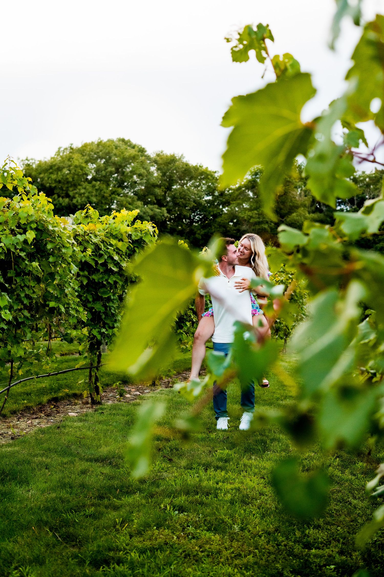 A romantic couple shares a tender moment among lush green grapevines in a vineyard on a sunny afternoon.