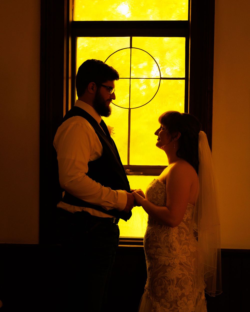 Silhouettes of a couple dancing together in front of a yellow-lit window creating a romantic backlit scene.