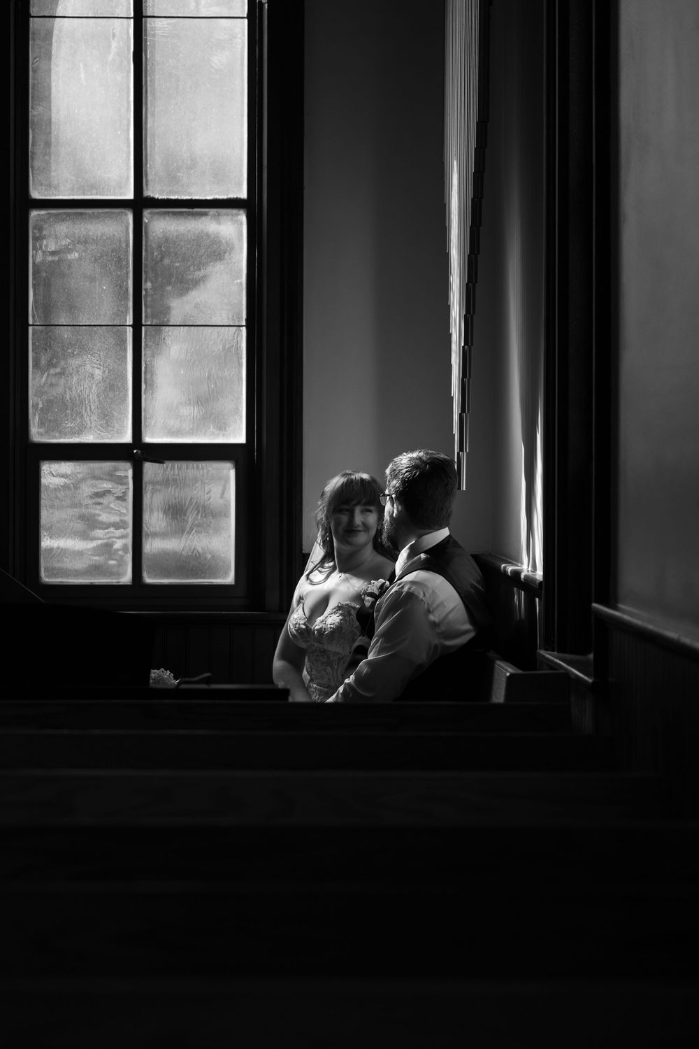 Black and white photo of a cat silhouetted in a window frame, creating a moody atmospheric composition.