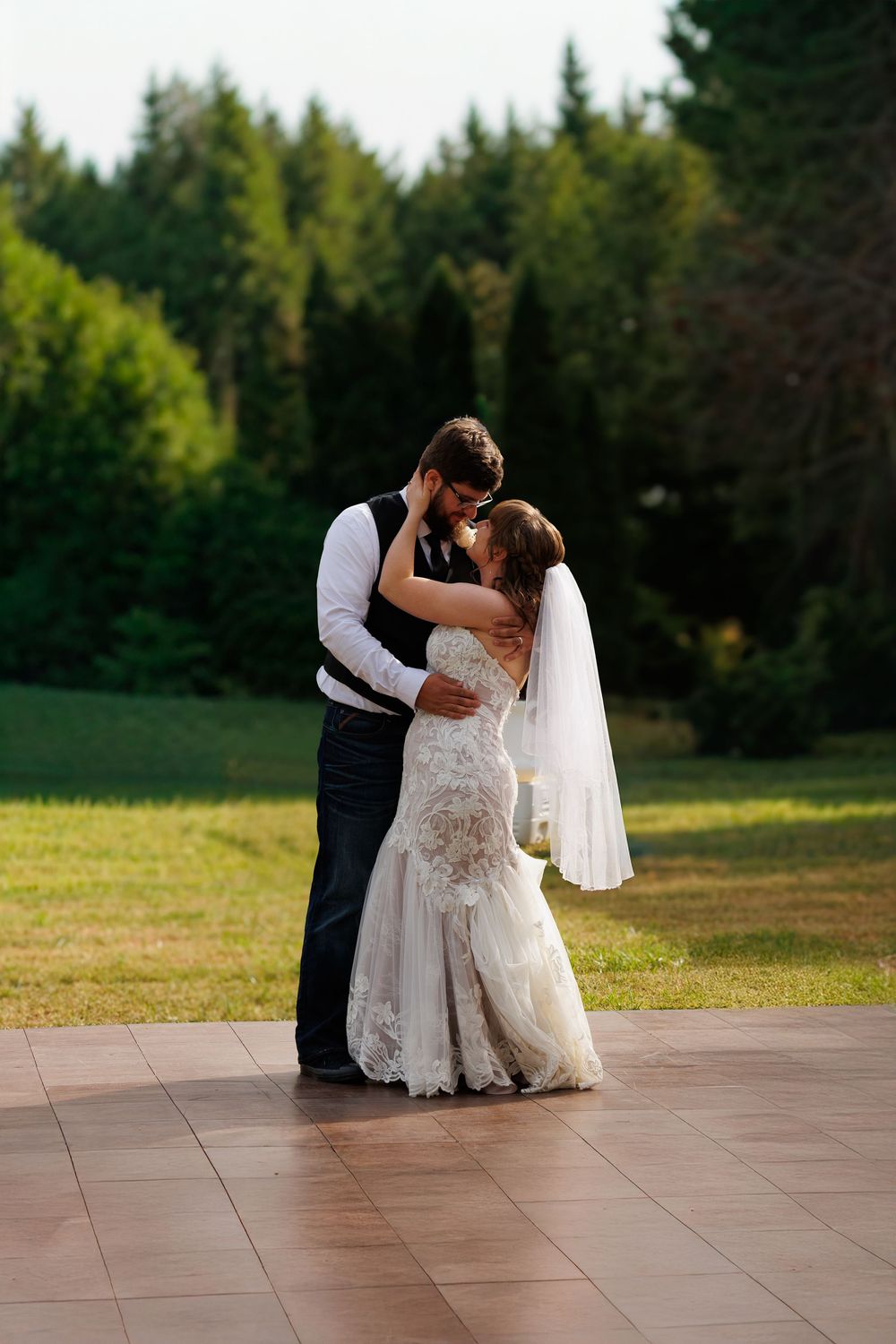 A couple dances together on an outdoor terrace with a forest backdrop during golden hour.