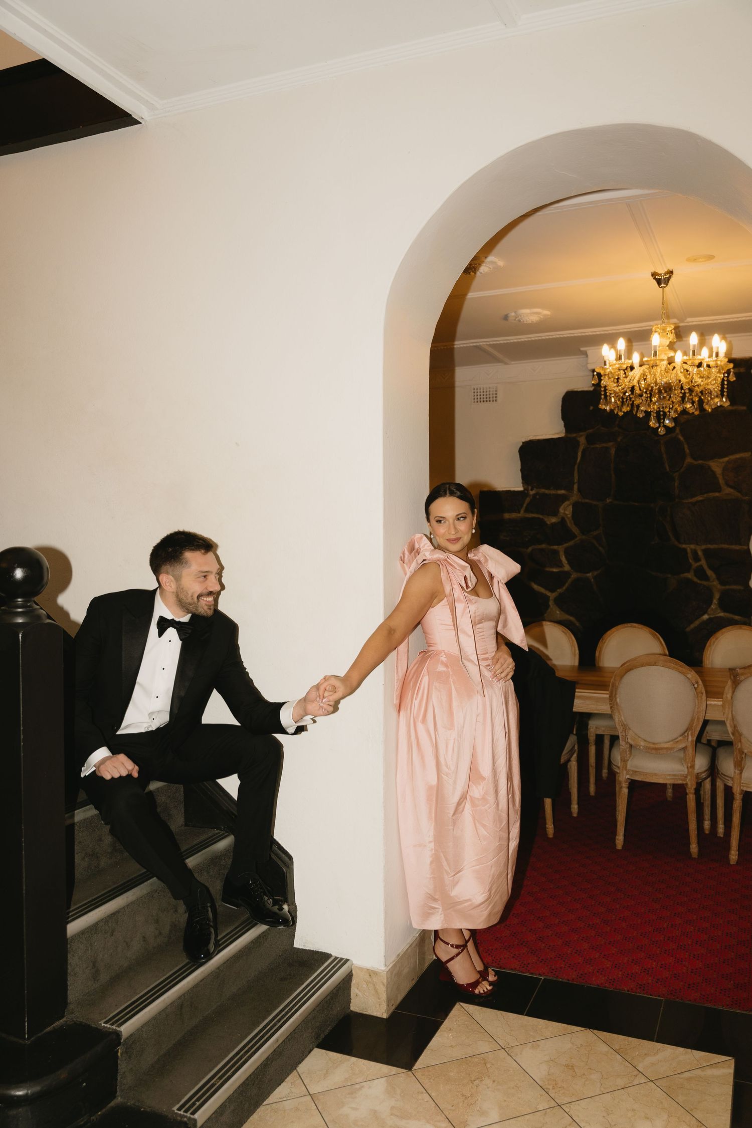 A playful sequence of dance moves between two people in formal attire on a carpeted floor with arched doorways.