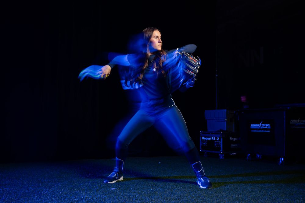 Performer in bright blue costume strikes dramatic pose on dark stage.