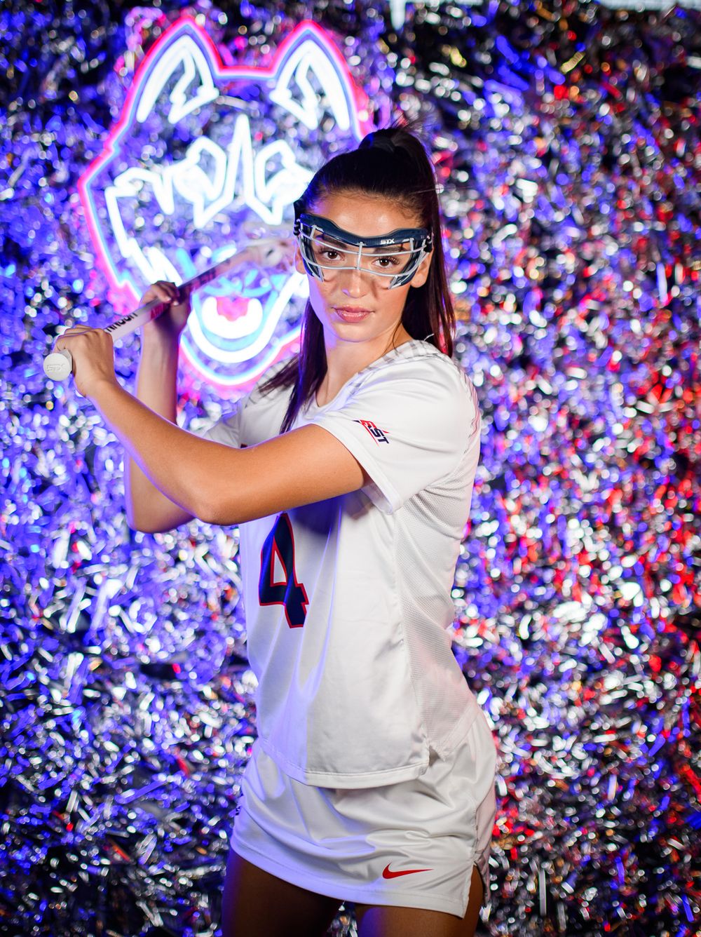 UConn lacrosse athlete poses for photo with neon lighting and confetti background.