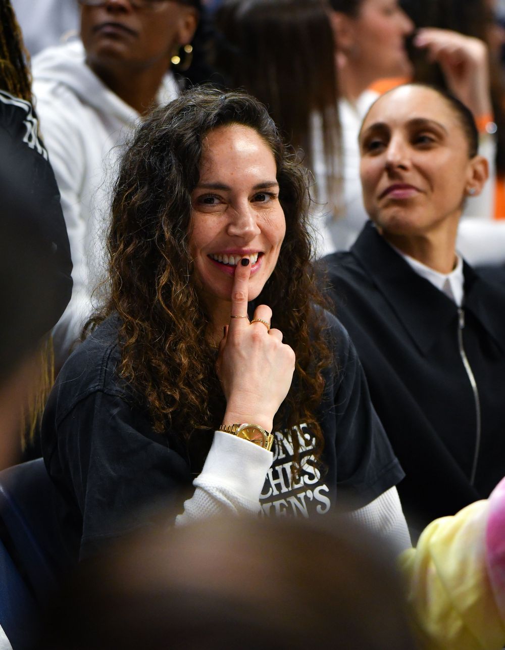 Sue Bird watches intently during sporting event from crowd seating.