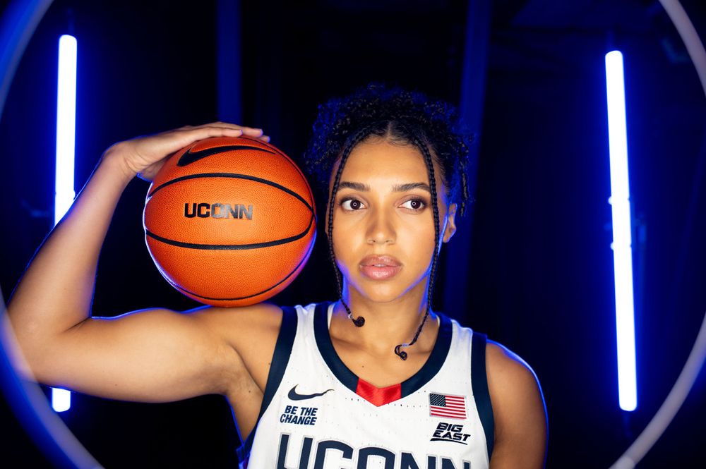 UConn athlete, Azzi Fudd, holds basketball in photo shoot with blue neon lighting.