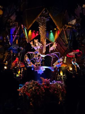A colorful nighttime display of robotic birds and tropical plants with vibrant lighting effects at a theme park attraction.