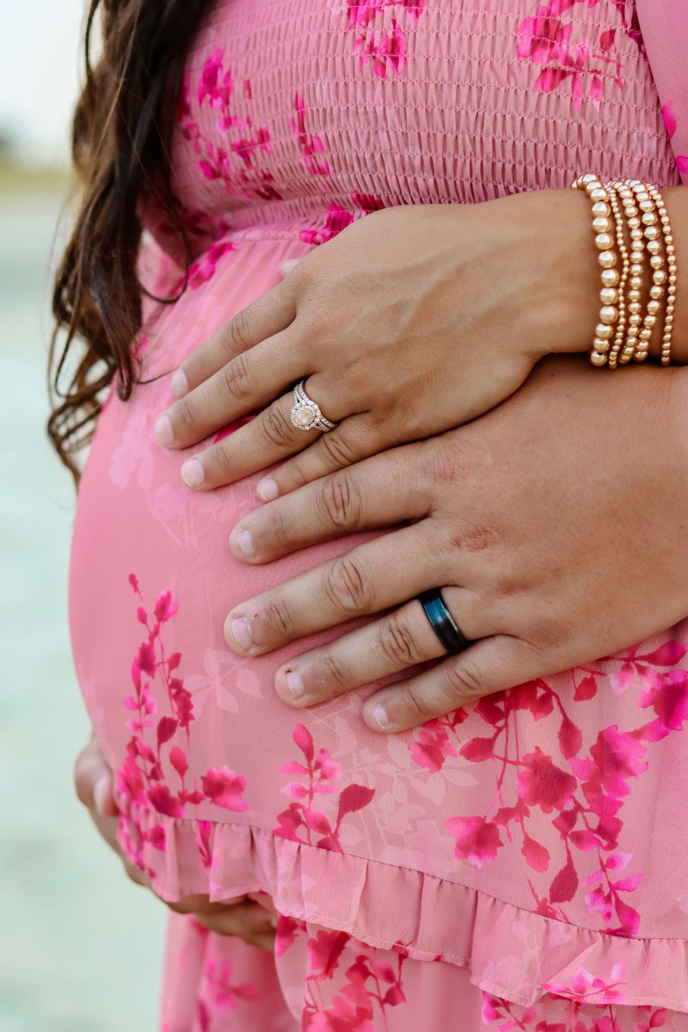 Close-up of hands with wedding rings resting on pink floral maternity dress.
