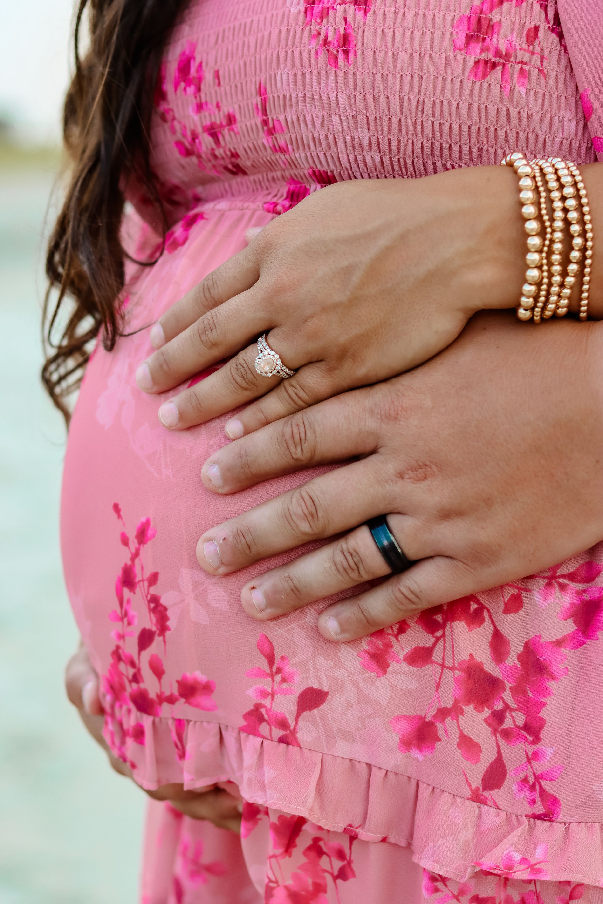Close-up of hands with wedding rings resting on pink floral maternity dress.