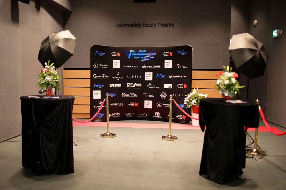 A professional event setup with step-and-repeat backdrop, velvet ropes, floral arrangements and lighting for photo opportunities.