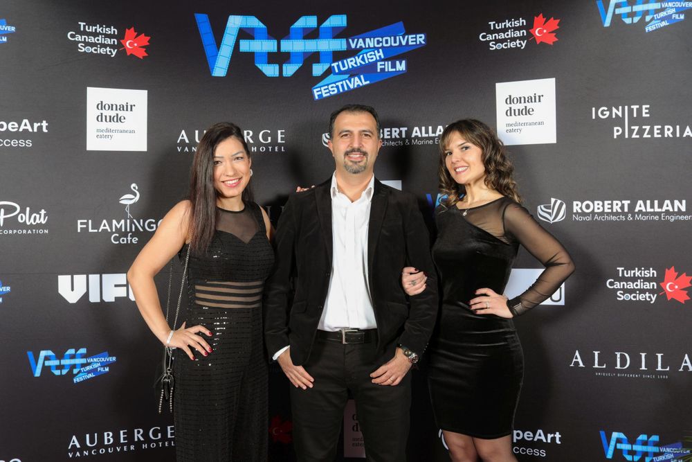 Three people pose together at a formal event with blue VAFF signage and sponsor logos visible in the background.