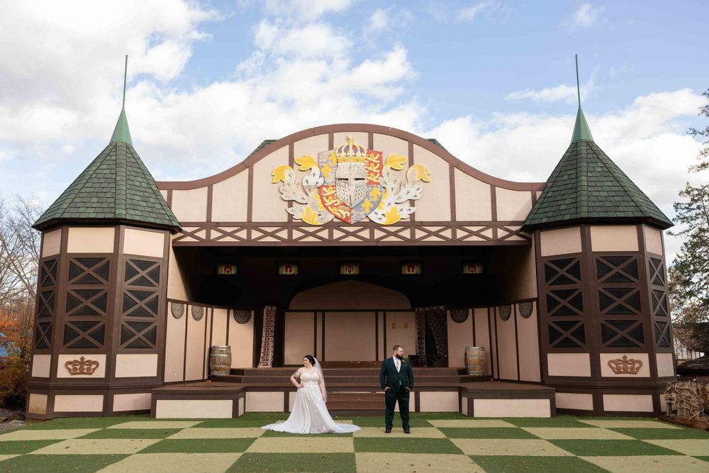 Two people standing in front of a rustic pavilion with green spires and decorative art deco facade on a sunny autumn day.